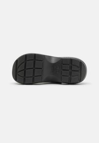 Semelle de chaussure en caoutchouc noir avec des motifs de grip texturés, présentant plusieurs semelles et un logo embossé dans la zone de l'arche.