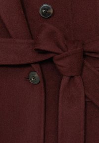 Bordo vilnos mišinio paltas su diržu juosmeniui ir juodais sagais, turintis švelnią tekstūrą ir struktūrizuotą, siuvinėtą dizainą.