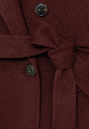 Burgundi gyapjú keverék kabát, amelynek derékon megkötős és fekete gombos díszítése van, puha tapintással és formatervezett, szabott fazonnal rendelkezik.