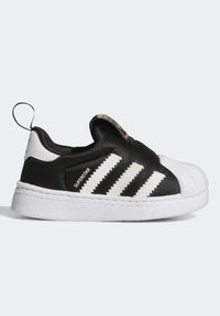 Černé slip-on tenisky s bílým špičkovým krytem, třemi bílými pruhy a textilním svrškem. Obsahují poutko na patě.