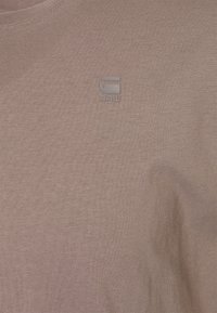 Tissu côtelé taupe brun avec un petit logo gris G-Star RAW imprimé près de la zone centrale de la poitrine d'un t-shirt.