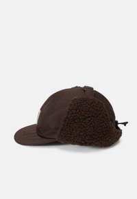 Cappello marrone con una soffice e morbida protezione per le orecchie in tessuto brunito. Il tessuto principale è elegante, con una piccola toppa logo sul lato.