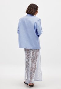 Svijetloplavi blazer s ležernim fitom, uparen s prozirnom bijelom čipkastom maksi suknjom. Izgled sadrži nježne teksture i elegantne uzorke.