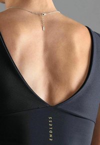 Schwarzes Sportoberteil mit tiefem V-Rücken-Design, aus glattem Stoff und goldener Schrift, die "ENDLESS" liest. Silberne Kettendetails am Hals.