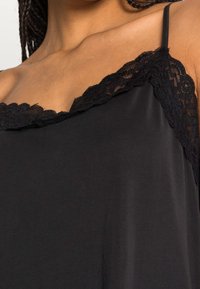Camisola nera con pizzo lungo il collo e spalline sottili, realizzata in un materiale liscio e leggero.