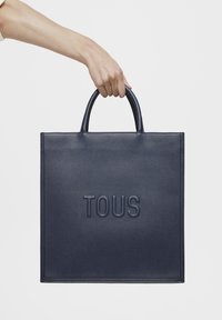 Nawojowana torba skórzana w kolorze granatowym z wytłoczonym logo "TOUS", o strukturze sztywnej, z podwójnymi uchwytami i teksturowanym wykończeniem.
