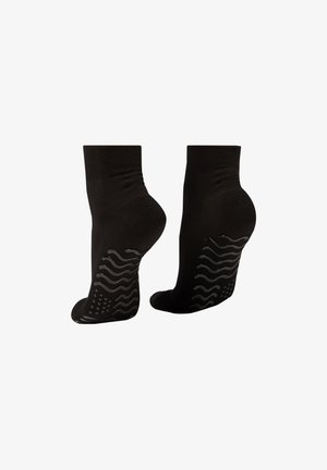 Zwarte enkelkousen met een gestructureerd siliconen grippatroon op de zolen, glad materiaal en een strakke pasvorm rond de enkel.