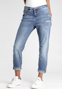 Vaaleansiniset farkut, joissa on rento leikkaus, käännetyt lahkeet, nyörivyö ja useita taskuja. Kulutettu yksityiskohtaus lisää tekstuuria.