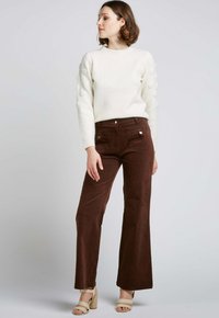 Pull en tricot blanc avec des manches bouffantes texturées, associé à un pantalon en velours côtelé marron évasé avec des poches avant et des accents de boutons.