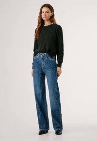 Camisola preta de malha com decote redondo e punhos canelados, combinada com jeans azuis de cintura alta, apresentando um padrão subtil e corte de perna direita.