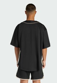 Čierny športový dres z sieťoviny s krátkymi rukávmi, ktorý má kontrastný biely golier a bočné pruhy, spolu s čiernymi šortkami, ktoré majú biely lem.