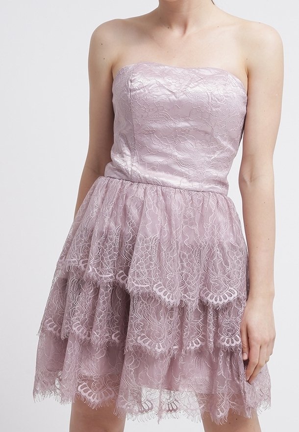 Ärmlös lila klänning med ett lager av spetskjol och slät satinklänning, bärs av en person med bara axlar och synliga armar.