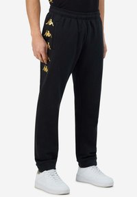 Zwarte sweatpants met gouden logo-accenten aan de zijkant, elastische tailleband en zijzakken. Gemaakt van zachte stof.