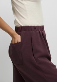 Burgundi värvi dressipüksid pehme tekstuuri, elastse vöökoha, küljetaskute ja volditud detailidega, kombo koos sobiva kreemja pluusiga.