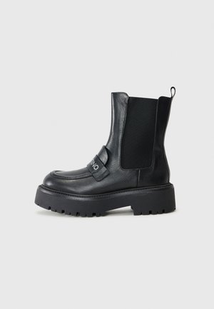 Black ankle boots made of leather featuring elastic side panels, a chunky sole, and a strap with a silver logo detail.