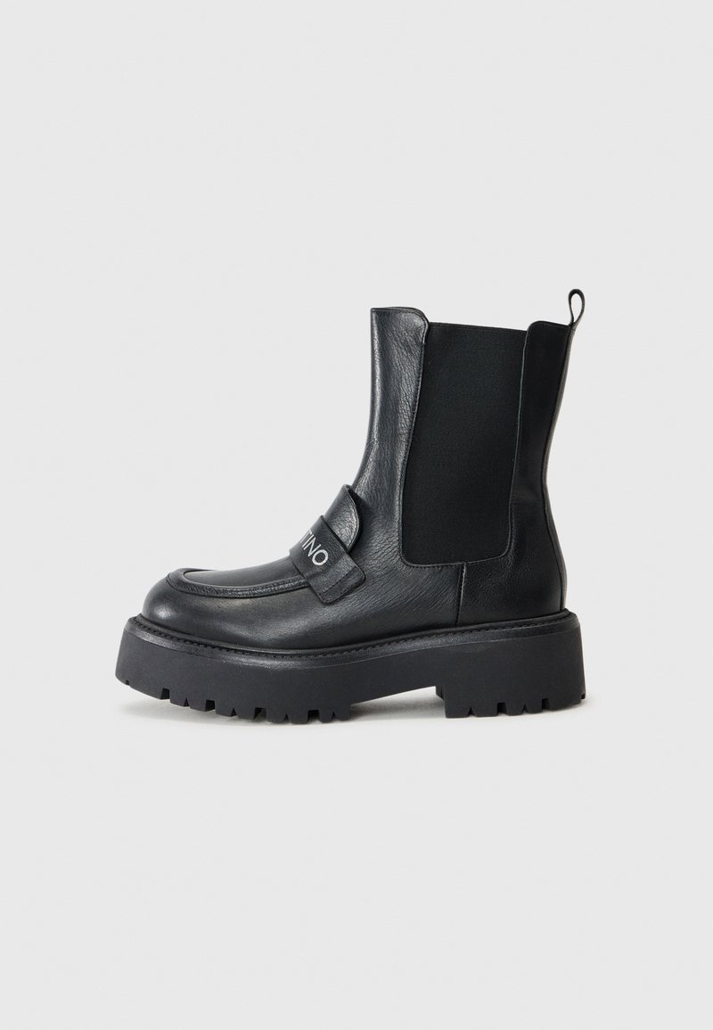 Black ankle boots made of leather featuring elastic side panels, a chunky sole, and a strap with a silver logo detail.
