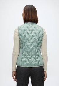 Svetlozelená prešívaná vesta s prídavkom. Má stojačik, bezrukávový strih a hladkú, lesklú textúru.