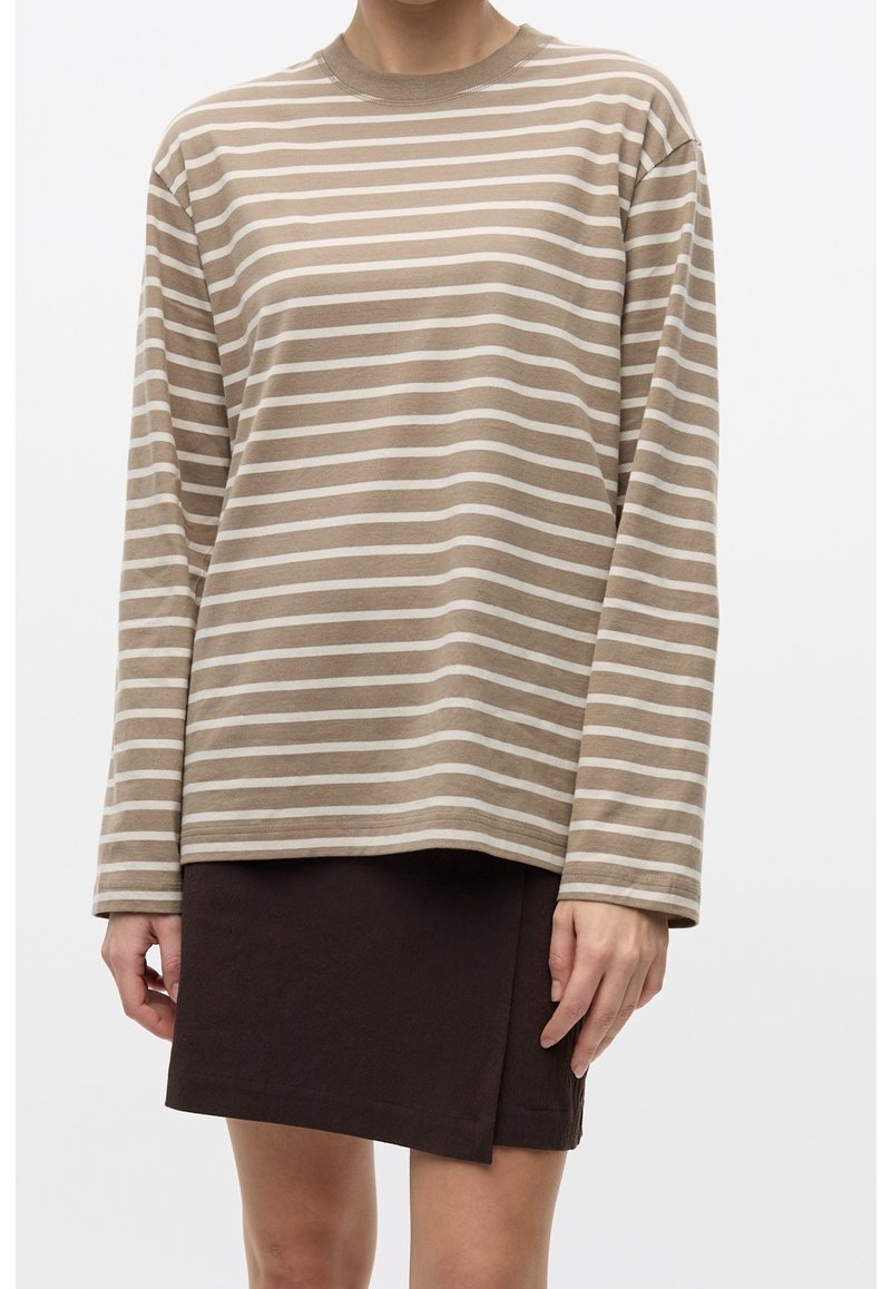 Camisa beige de manga larga con rayas horizontales blancas, cuello redondo, ajuste relajado, combinada con una mini falda marrón oscuro.