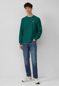 Turkusowa koszula z długim rękawem z białym akcentem na kołnierzyku, slim fit, zestawiona z niebieskimi dżinsami i jasnymi trampkami, prezentująca swobodny styl.