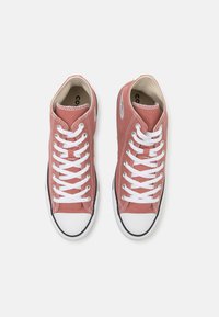Rosa kanvas sneakers har hvite snørebånd, en svart gummisåle og rund tå. Innvendig fôr er beige; merkevarenlogoen vises på siden.