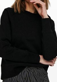 Sudadera negra de corte relajado, con puños y dobladillo de canalé. Tejido suave con mangas raglán, combinada con una falda de estampado de cebra en negro y gris.