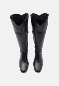 Čierne kožené čižmy po kolená so štvorcovou špičkou, zdobené vrchným okrajom so zubatým vzorom a bočným zipsom, hladká textúra a minimálne detaily.