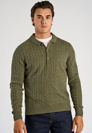 Olijfgroene kabelgebreide trui met een kraag, twee knopen en geribbelde manchetten en zoom. Draagt over een wit overhemd.