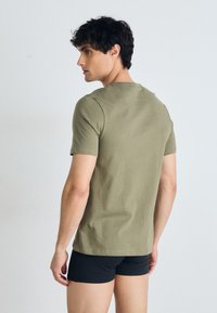 Olivgrünes, tailliertes T-Shirt aus Baumwolle, kurze Ärmel, runder Halsausschnitt, glatte Textur, keine sichtbaren Muster oder Akzente, getragen mit schwarzen Shorts.
