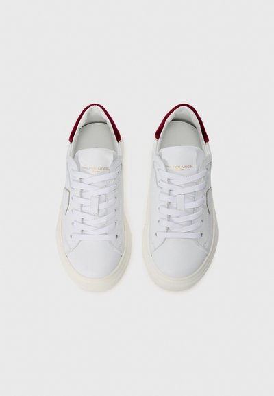 Weiße Leder-Sneaker mit burgunderrotem Wildlederakzent an der Ferse, flachen weißen Schnürsenkeln und einer strukturierten cremefarbenen Gummisohle. Minimalistisches Design.