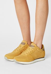 Gule sneakers med mesh-tekstil og ruskindsdetaljer, som har en tekstureret overflade og hvidspraglede ydersål. Snørelukning med polstret krave.