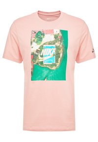 Camiseta de algodón rosa claro con un estampado aéreo colorido de una piscina, con el logo de "NIKE" en azul destacado.