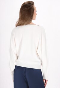 Witte gebreide trui met een ronde halslijn, verlaagde schouders en geribbelde zoom. Gecombineerd met marineblauwe broek, wat zorgt voor een relaxte pasvorm en een soepele textuur.