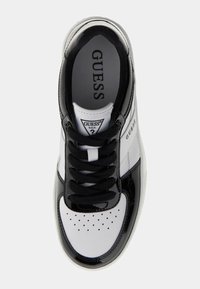 Czarno-biały sneaker z połyskującym wykończeniem, posiadający perforowany przód, czarne sznurowadła oraz logo po boku i na języku.