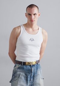 Hvit ribbet tank topp med liten hodeskallegrafikk, parret med falmede blå denimshorts og et brunt belte med en gull "MOSCHINO" spenne.