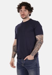 T-shirt azzurro scuro a maniche corte con scollo tondo e un logo discreto sul petto, realizzato in un morbido misto cotone. Abbbinato a jeans in denim.