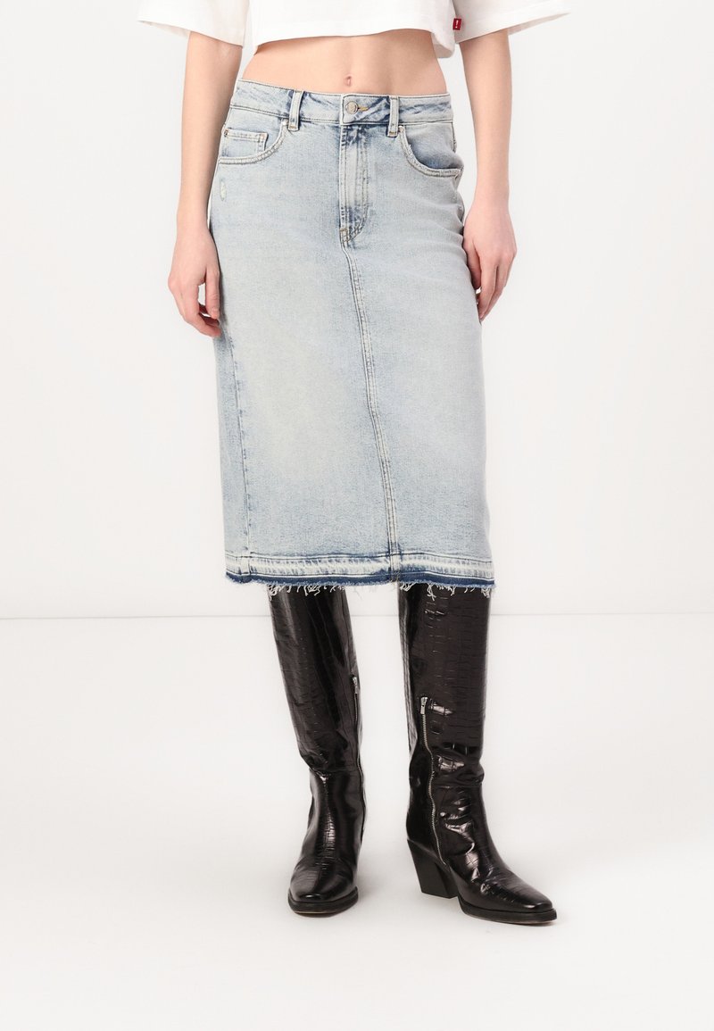 Lyseblå denim midi-skjørt med frynset kant og fem-lomme-design, kombinert med svarte knelengde støvler med teksturfinish.