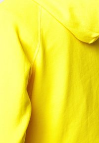 Tejido de sudadera amarilla con una textura suave. Presenta una capucha y detalles de costura visibles, mostrando un color sólido vibrante.