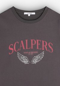 T-shirt en coton gris avec le mot "SCALPERS" en rouge, accompagné d'un graphique d'aile en dessous et de "ÉTAT DE LIBERTÉ EST. 2018" en blanc.