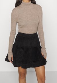 Ljusbrun ribbad polotröja kombinerad med en svart manchesterskjol med veckade detaljer och en utsvängd silhuett.