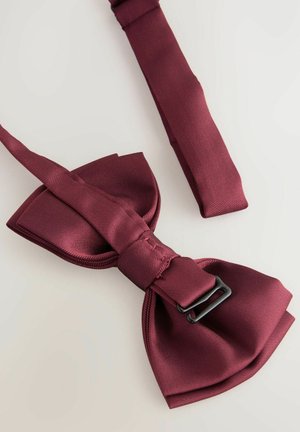Burgundi selyem csokornyakkendő sima felülettel, középső csomóval és állítható pántokkal. Fekete fém csat részlet tartozik hozzá.