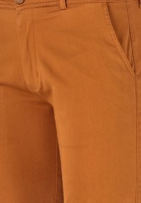 Braune Baumwollhose mit glatter Textur, ausgestattet mit einer frontalen Tasche und einem klassischen Knopfverschluss. Der Stoff hat einen leichten Stretchanteil.