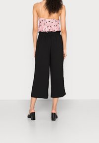 Pantalon noir à jambes larges avec taille élastique, associé à un haut rose brodé de fleurs. Tissu lisse avec une coupe décontractée. Sandales noires à talons blocs.