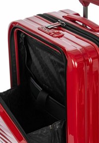 Valigia rigida rossa con scomparto frontale aperto che mostra un interno nero con tasche con zip e una manica per laptop.