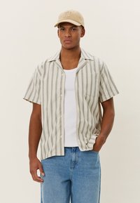 Stripet kortermet skjorte i lys beige med grønne striper, lett stoff, knappet foran, enkelt brystlomme, kombinert med blå jeans.