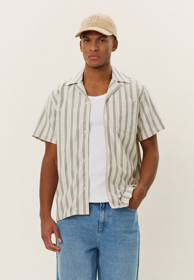 Stripet kortermet skjorte i lys beige med grønne striper, lett stoff, knappet foran, enkelt brystlomme, kombinert med blå jeans.