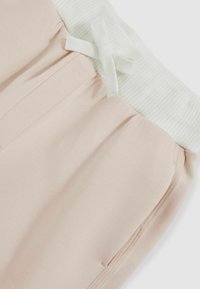 Šviesiai rožiniai sportiniai džinsai su banguota balta juosta, puošti dekoratyvine užkaba ir šoninėmis kišenėmis didesniam funkcionalumui. Minkštas audinio tekstūra.