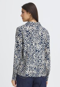 Blouse marine avec un motif crème abstrait, manches longues, col boutonné et coupe décontractée. Tissu lisse avec un subtil éclat.