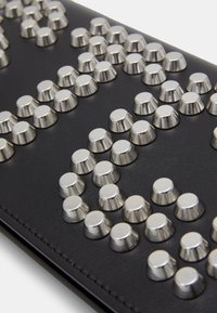 Svart läderyta detaljerad med glänsande silverplittar, arrangerade i ett mönster, som framhäver textur och strukturell design.