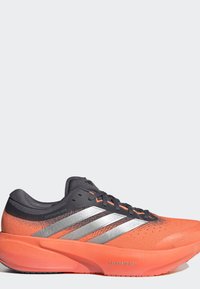 Πορτοκαλί και μαύρο παπούτσι τρεξίματος Adidas με ασημένιες ρίγες, μαύρα κορδόνια και χοντρή σόλα με την ένδειξη Dreamstrike plus, πλάγια όψη.
