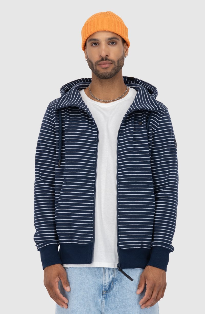 Felpa a righe navy e bianche con zip sul davanti, cappuccio regolabile e polsini a coste. Indossata sopra una semplice t-shirt bianca, abbinata a jeans chiari.